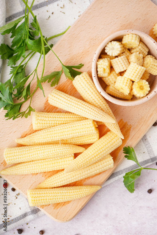 Wooden board with cut and whole canned baby corn cobs on light background