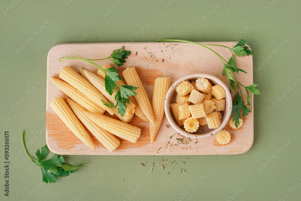 Wooden board with cut and whole canned baby corn cobs on olive background