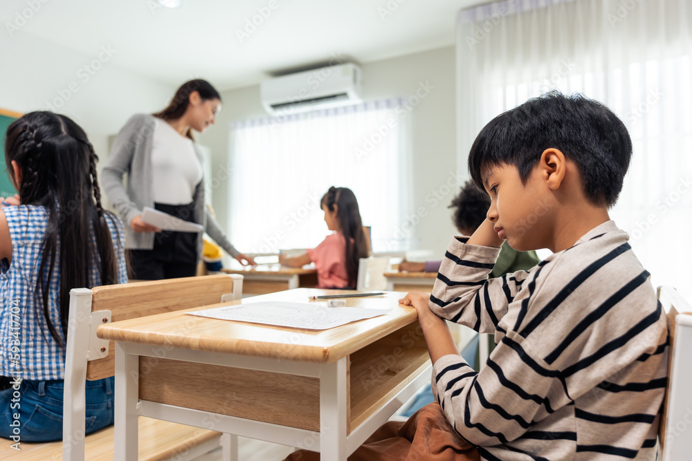 Asian young tired boy student doing an exam test at elementary school. 