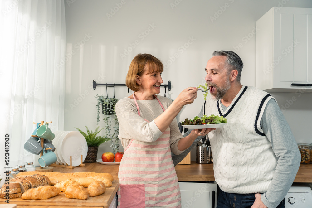 Caucasian senior elderly couple spend time together in kitchen at home. 