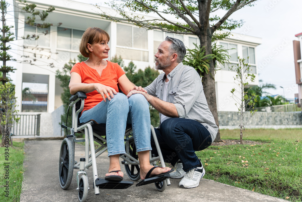 Caucasian senior woman support husband on wheelchair outdoor in garden.