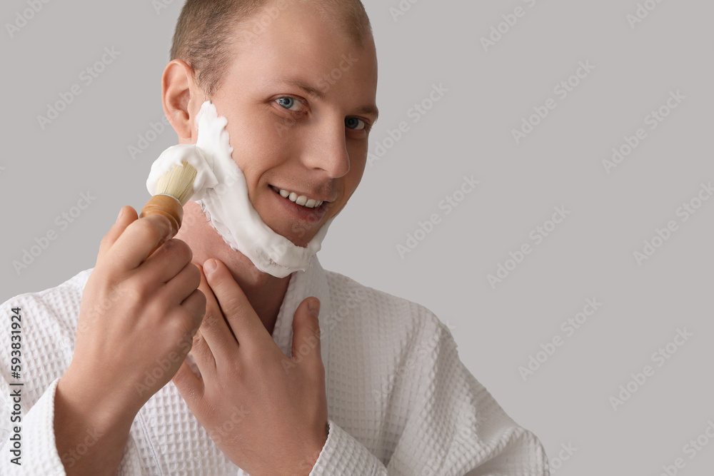 Young man applying shaving foam on face against light background