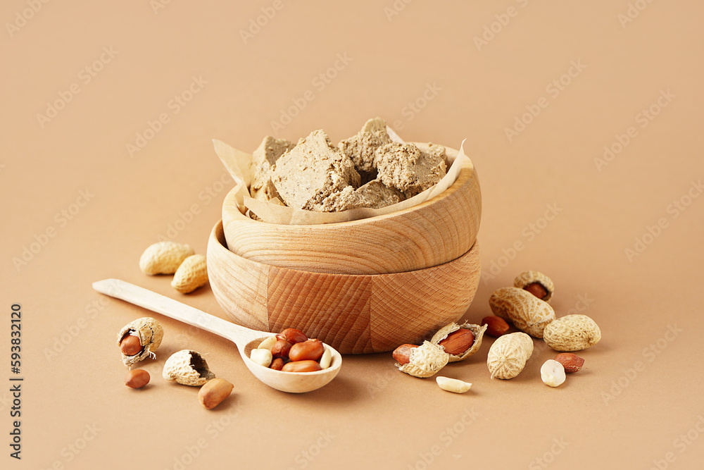 Wooden bowls of sweet halva and peanuts on color background