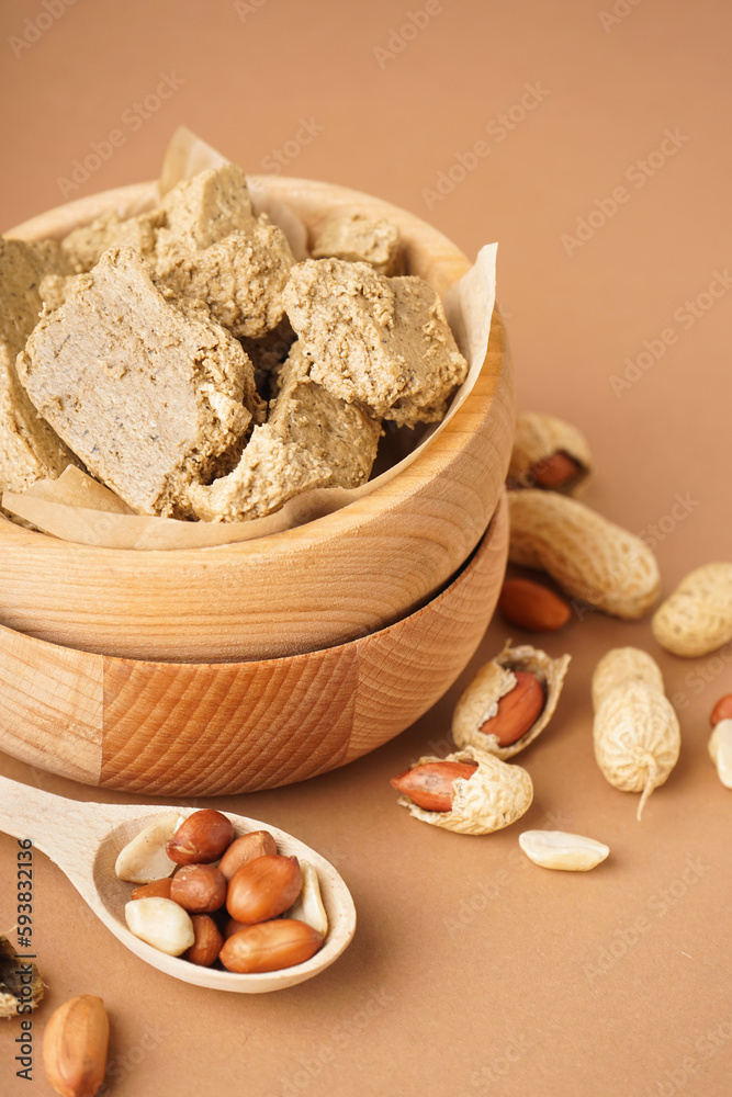 Wooden bowls of sweet halva and peanuts on color background, closeup