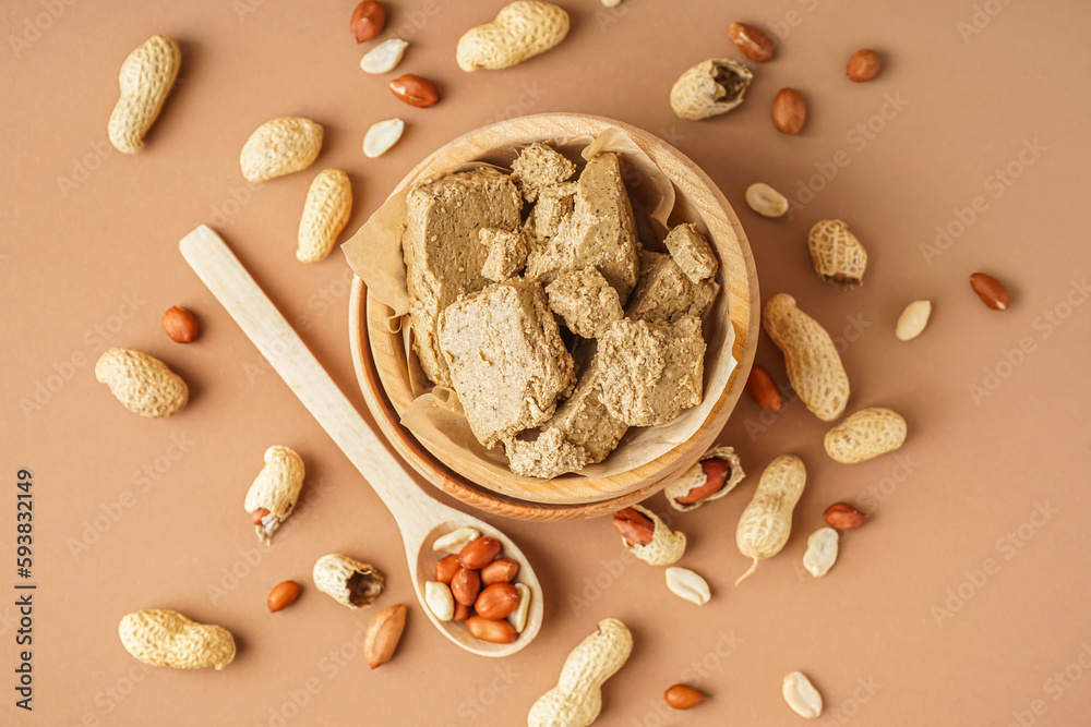 Wooden bowl of sweet halva and peanuts on color background