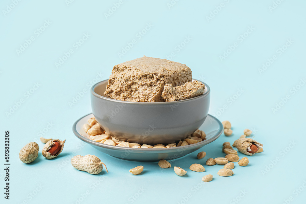 Bowl of tasty halva and peanuts on color background