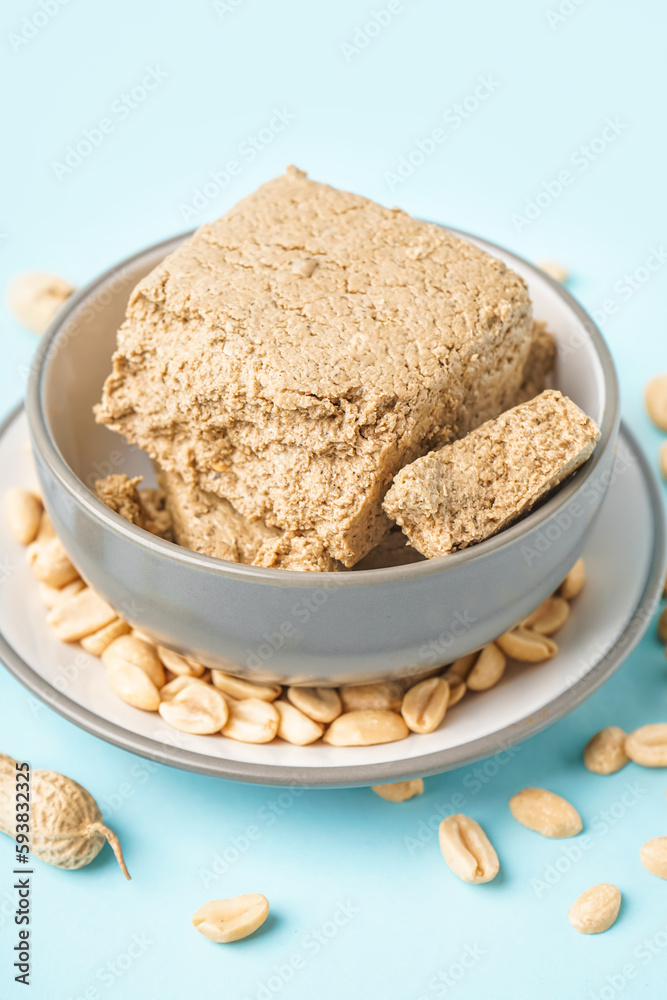 Bowl of tasty halva and peanuts on color background, closeup