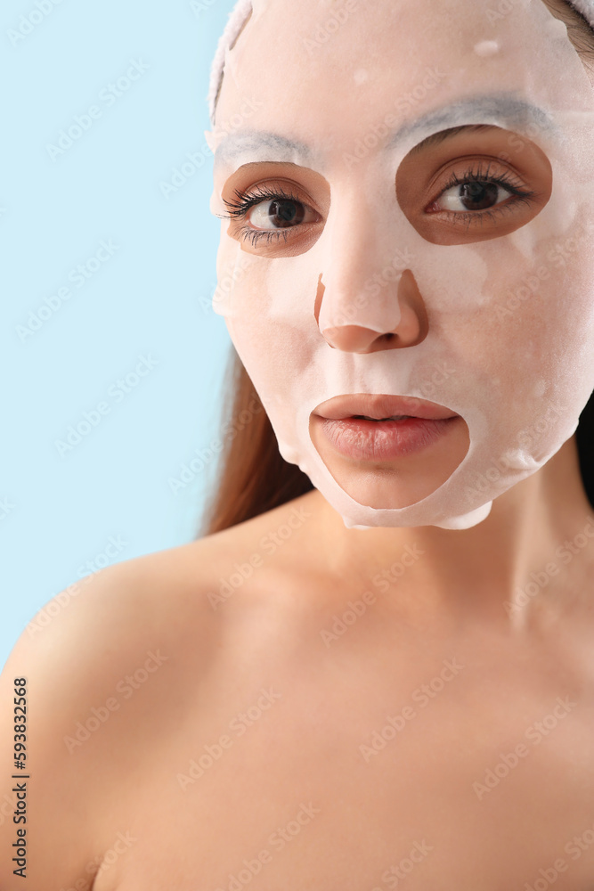 Young woman with sheet mask on blue background, closeup