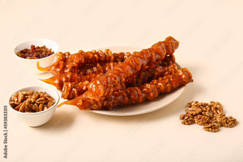 Plate with tasty churchkhela, raisin and walnuts on light background