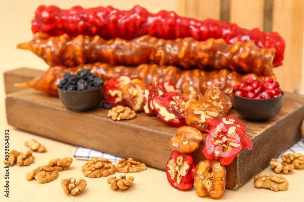 Board with delicious churchkhela and walnuts on beige background