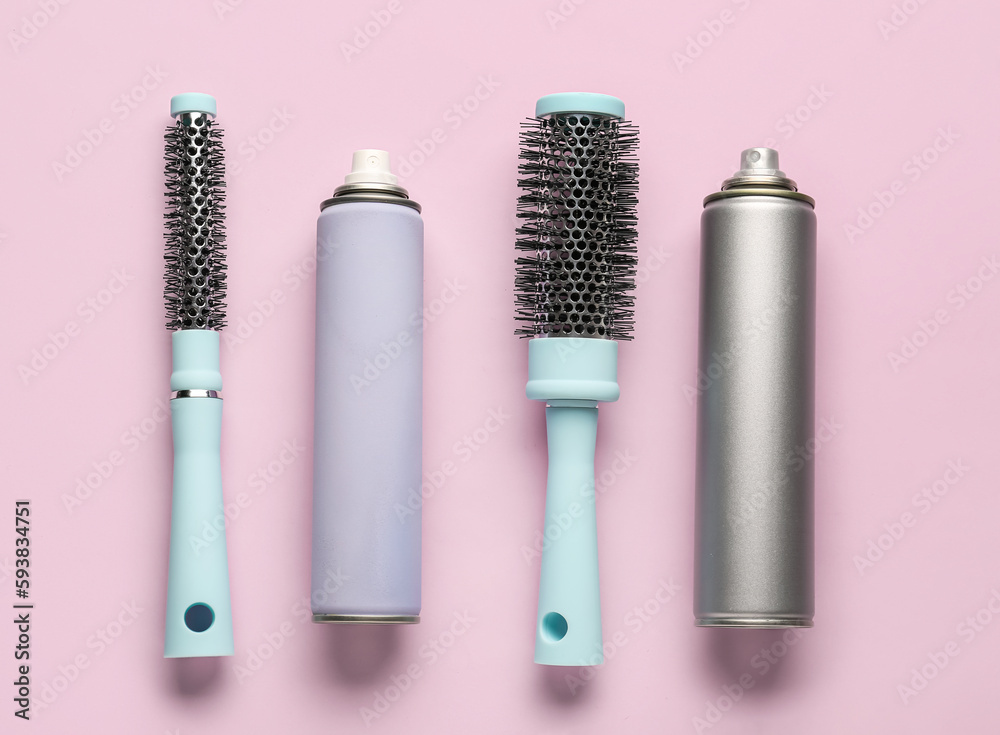 Bottles of hair sprays and brushes on color background