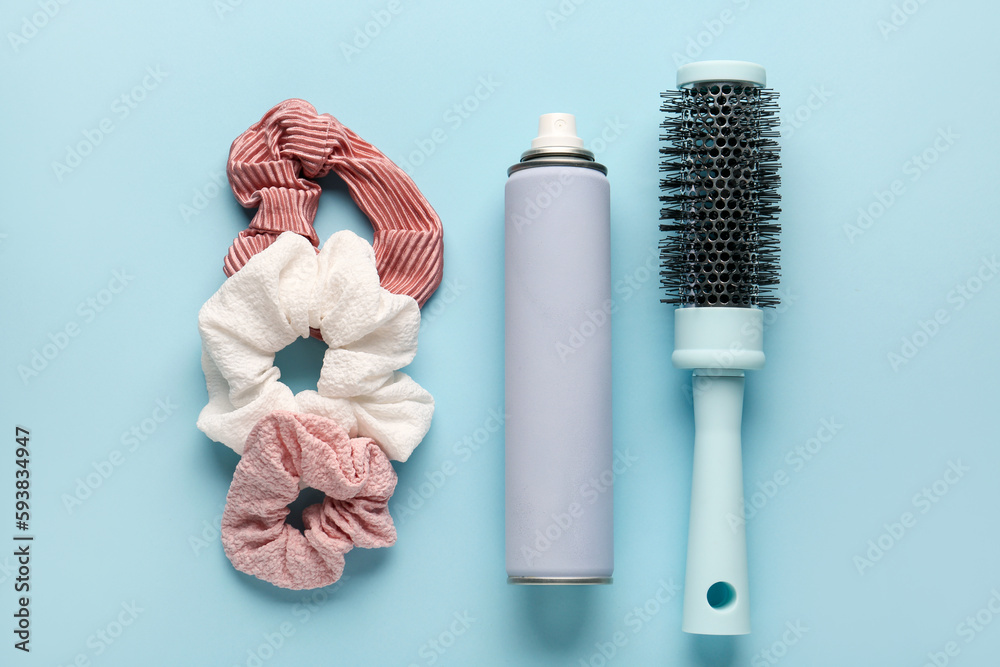 Bottle of hair spray, brush and scrunchies on color background