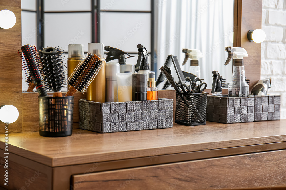 Organizers with different hair sprays and accessories on table in beauty salon