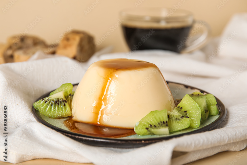 Plate with delicious pudding and kiwi slices covered by caramel syrup on beige background