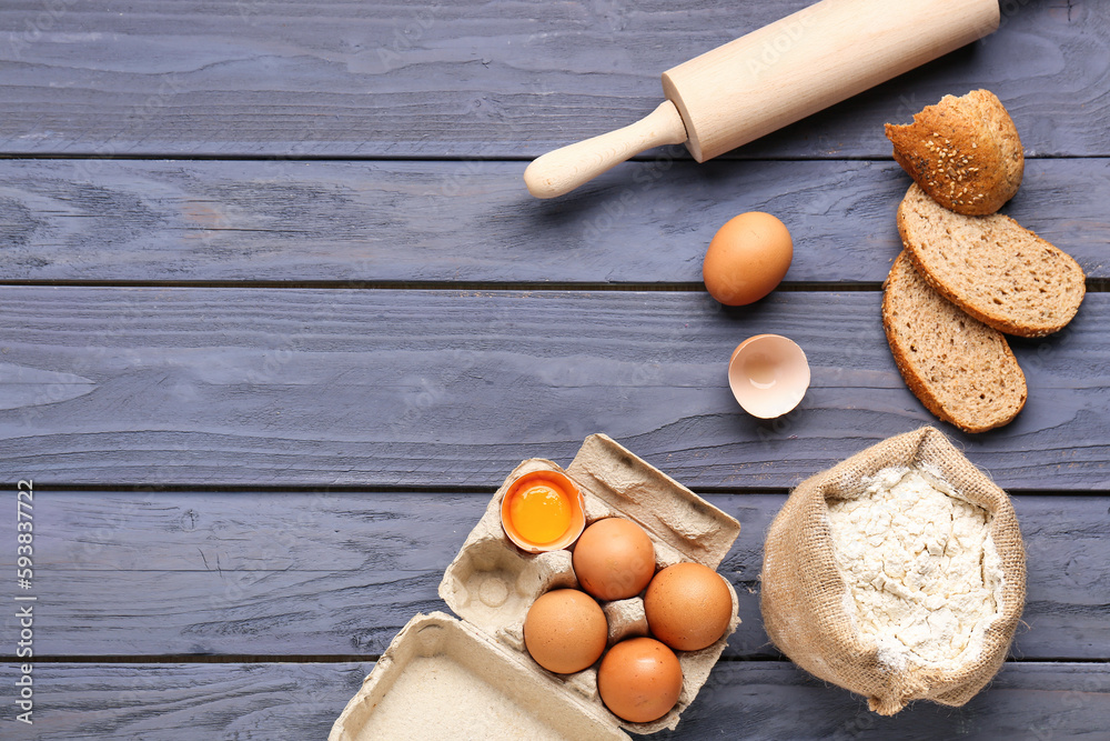 Composition with sack bag of wheat flour, eggs, bread and rolling pin on blue wooden table