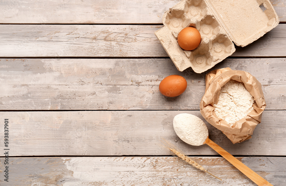 Composition with paper bag of wheat flour, spoon and eggs on grey wooden table