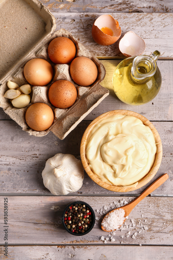 Bowl with tasty mayonnaise sauce and ingredients on grey wooden background