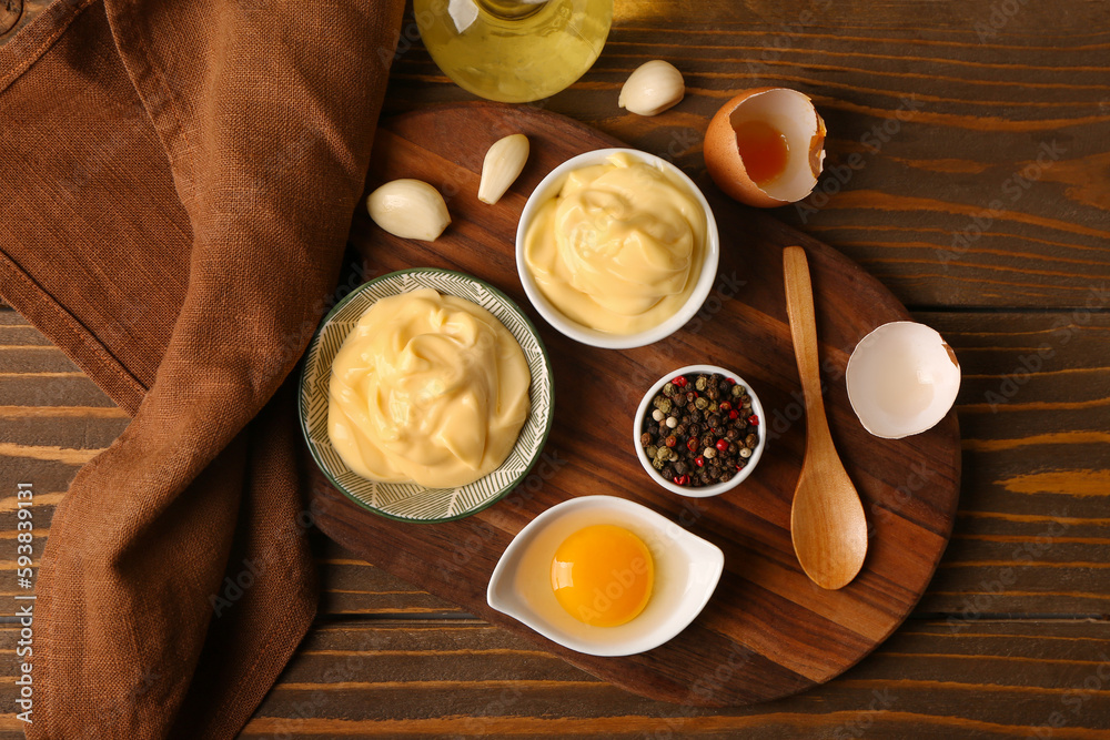 Bowls with tasty mayonnaise sauce and ingredients on wooden background