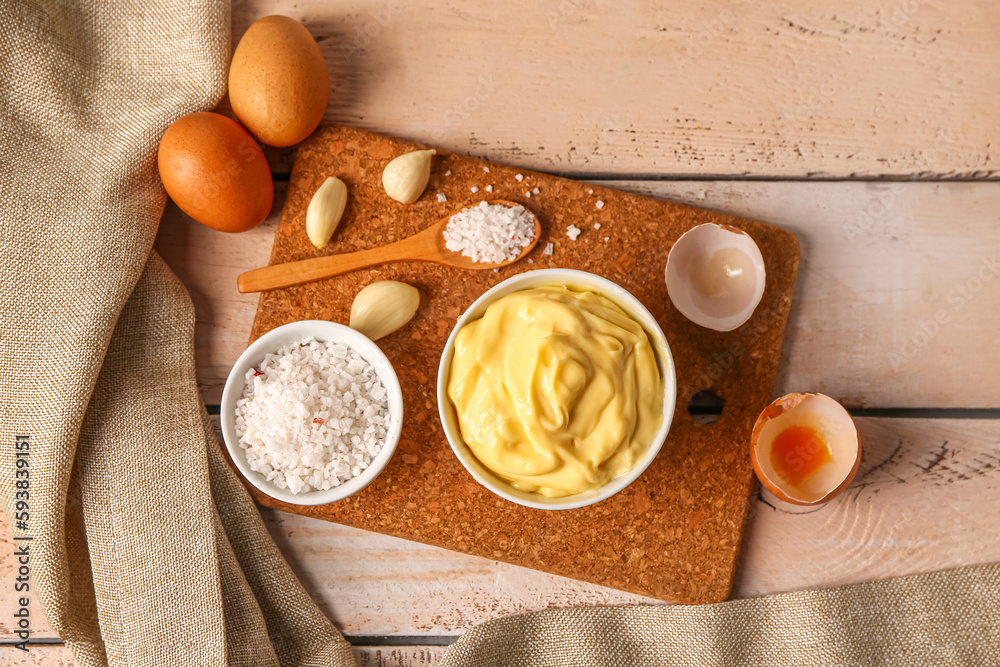 Bowl with tasty mayonnaise sauce and ingredients on light wooden background