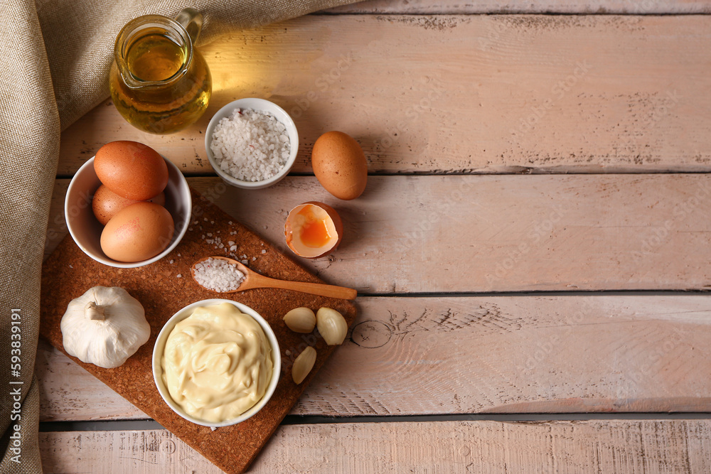 Bowl with tasty mayonnaise sauce and ingredients on light wooden background