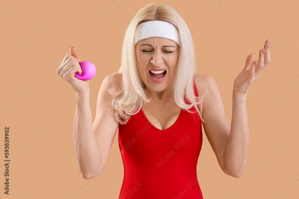 Angry mature woman with squeeze ball on beige background