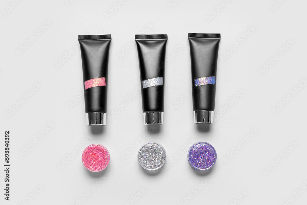 Tubes with jars of glitter on light background