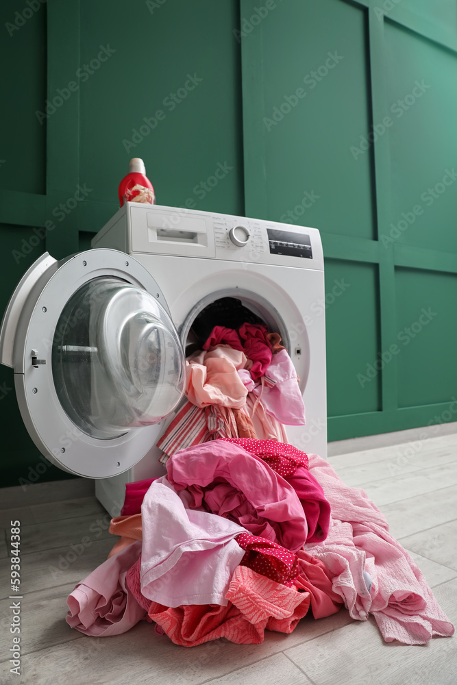 Washing machine with dirty clothes near green wall in laundry room