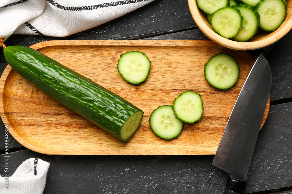 Board with fresh cut cucumber on dark wooden background