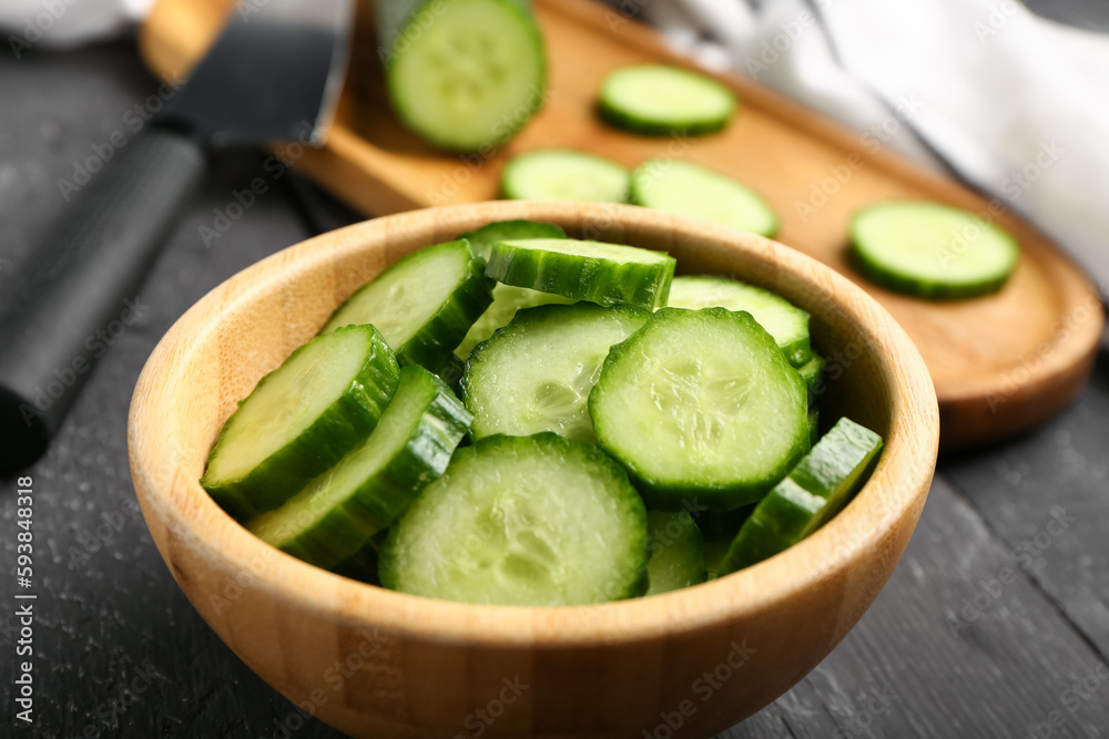 Bowl with fresh cut cucumber on dark wooden background, closeup