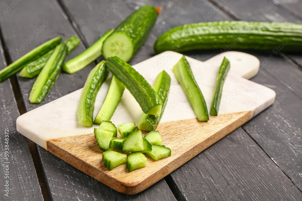 Board with fresh cut cucumber on dark wooden background