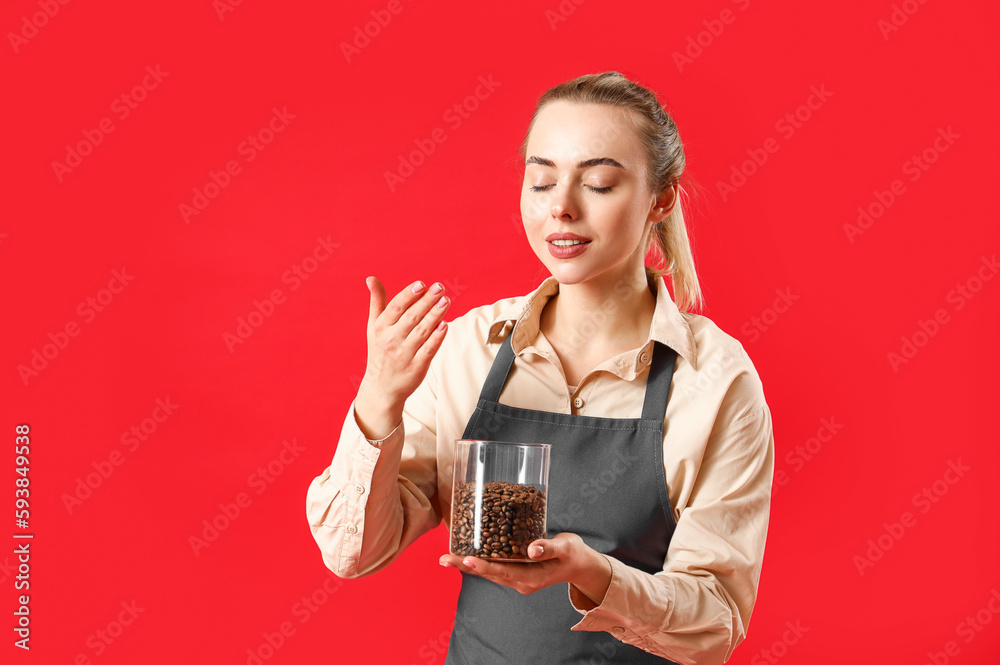 Young barista with jar of coffee beans on red background