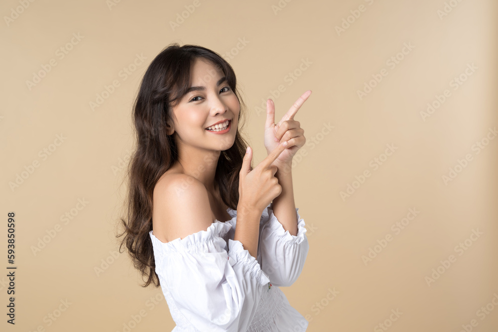 Young Asian woman pointing fingers up to empty space isolated brown color background