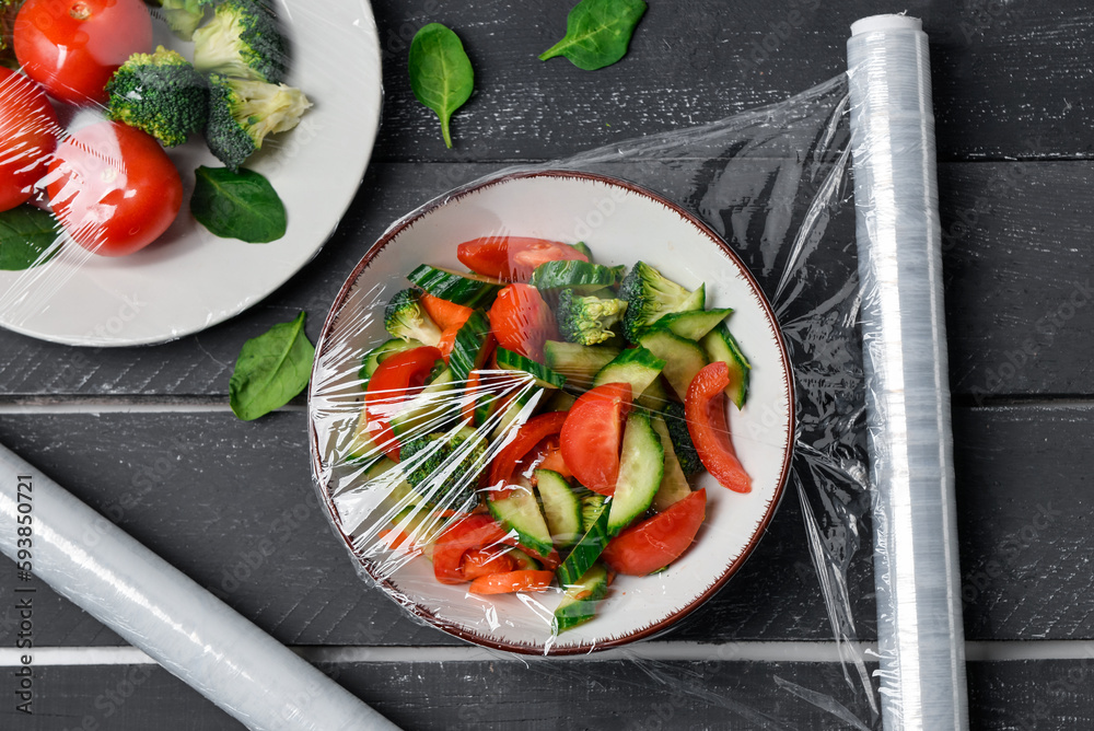 Bowl with salad wrapped with stretch wrap on dark wooden background