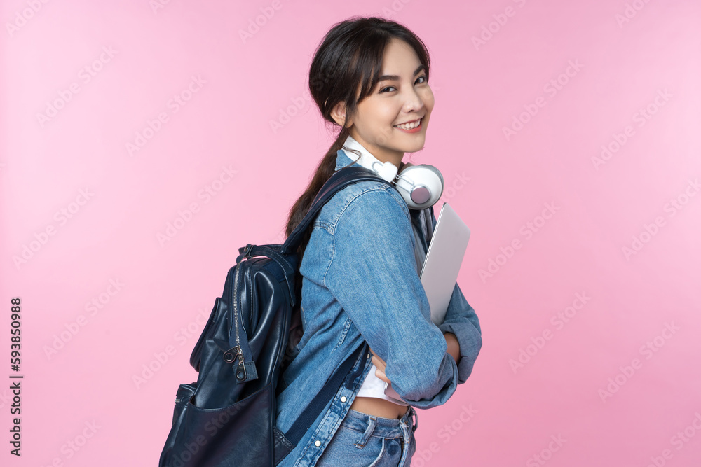 Portrait of smiling young Asian college student with laptop and backpack isolated over pink backgrou