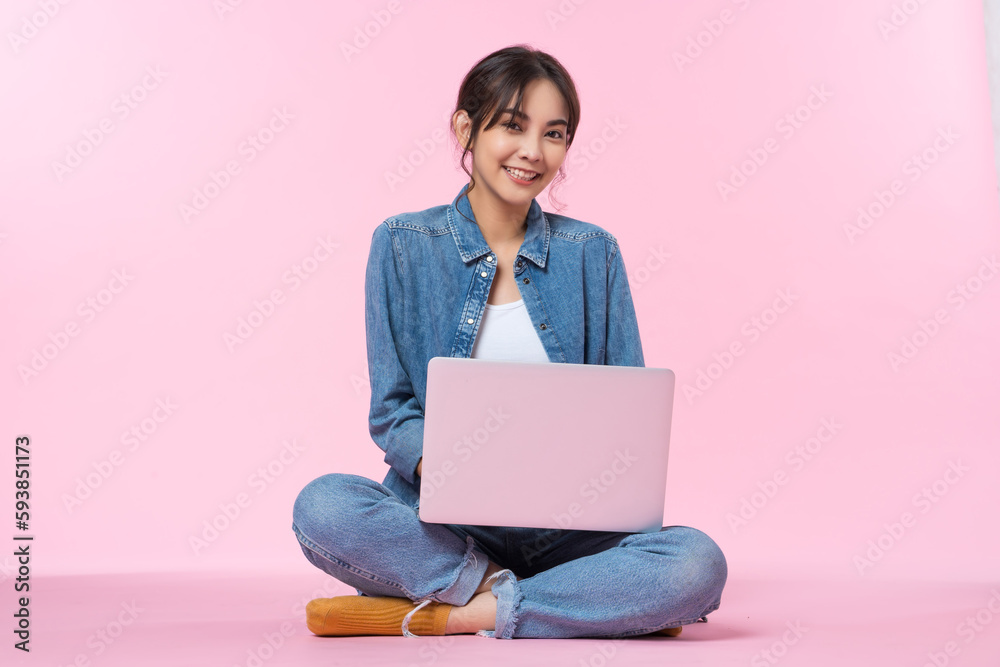 Young Asian college student sits cross-legged on floor working with a laptop computer, looking direc