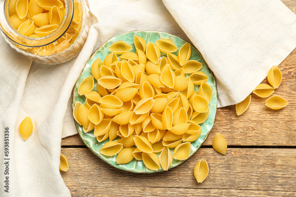 Plate with raw conchiglie pasta on wooden background