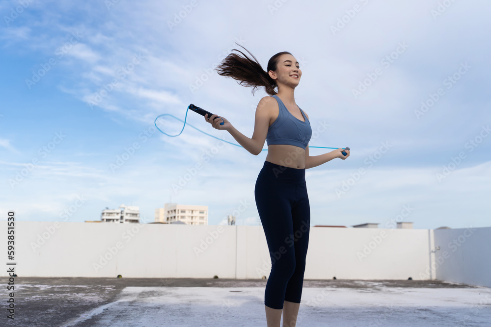 Young Asian woman with jump rope on rooftop. Fitness female doing skipping workout outdoors