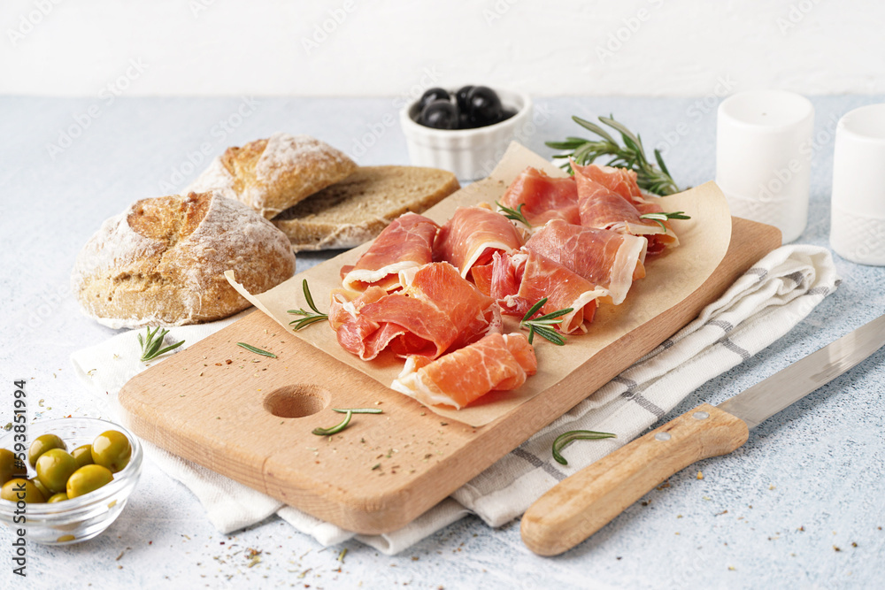 Wooden board with slices of tasty jamon on light background