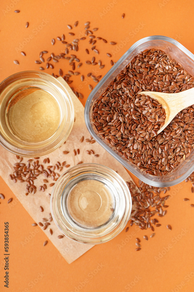 Glass with flax oil and bowl of seeds on orange background