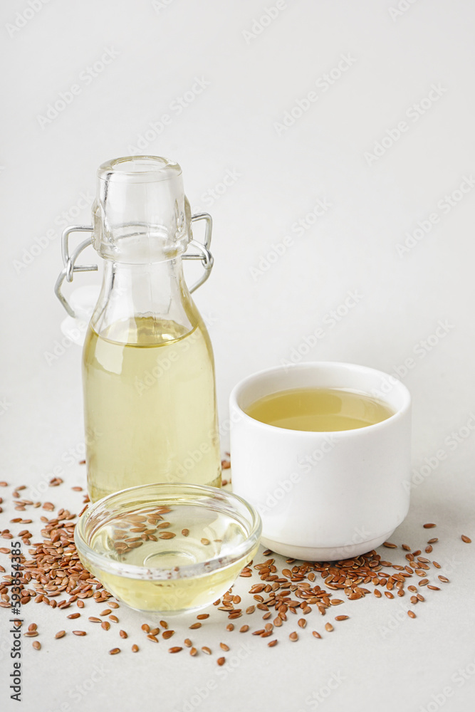 Bottle, bowl, glass with flax oil and seeds on light background