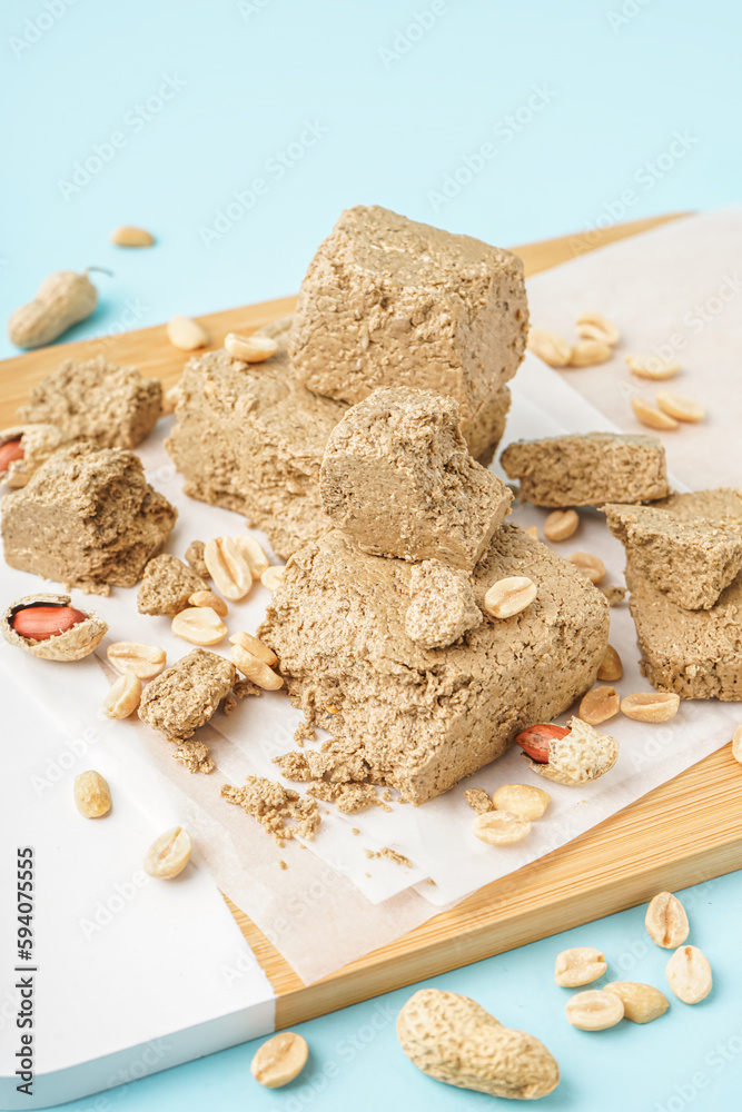 Wooden board of sweet halva and peanuts on color background, closeup