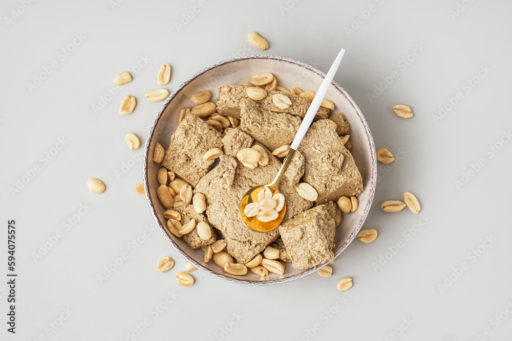 Bowl of tasty halva and peanuts on light background