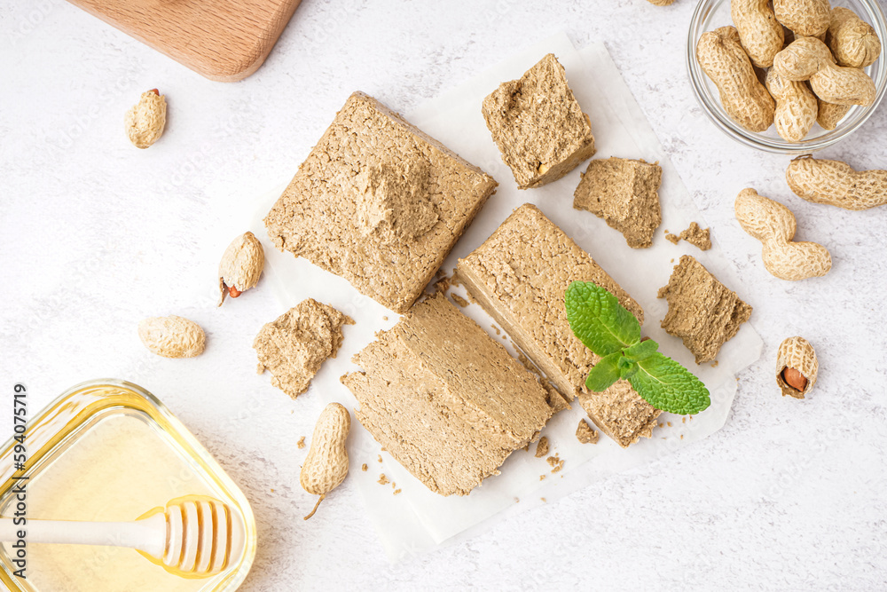 Pieces of tasty halva, peanuts and honey on light background