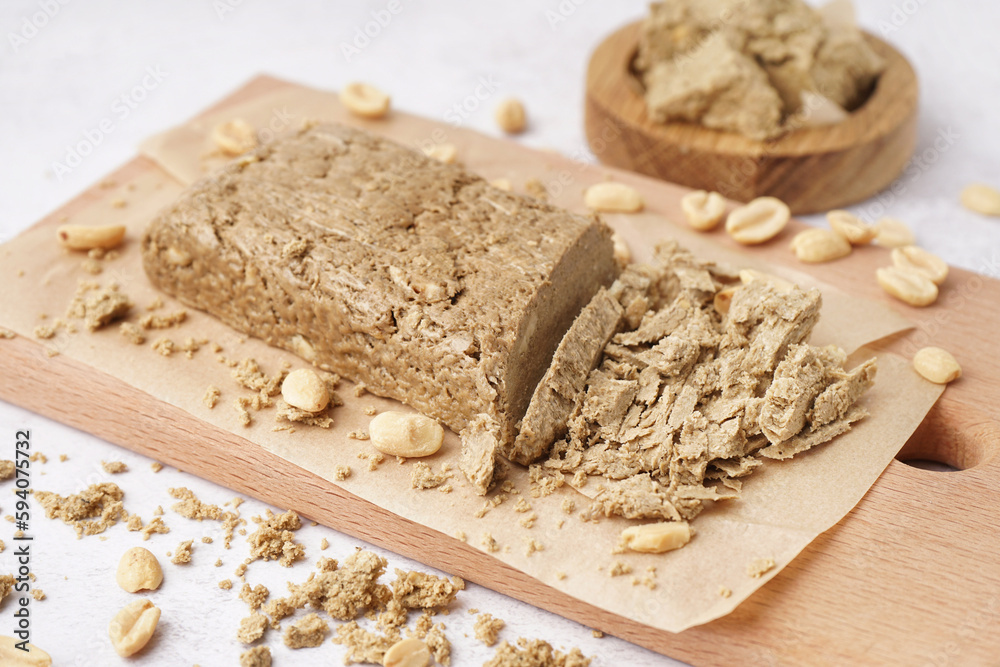 Wooden board of sweet halva with peanuts on light background, closeup