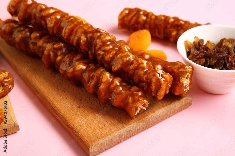 Wooden board with tasty churchkhela and raisin on pink background, closeup