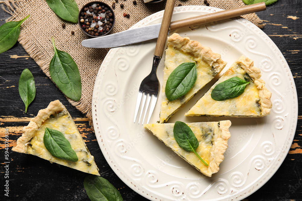 Plate with pieces of delicious quiche on black wooden background