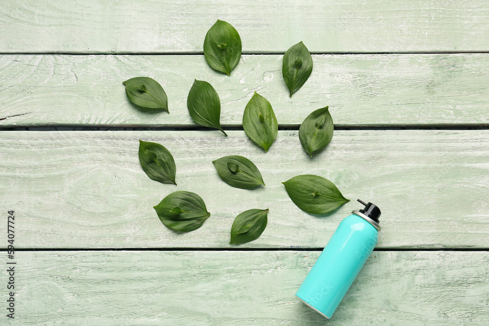 Composition with bottle of hair spray and leaves on light wooden background