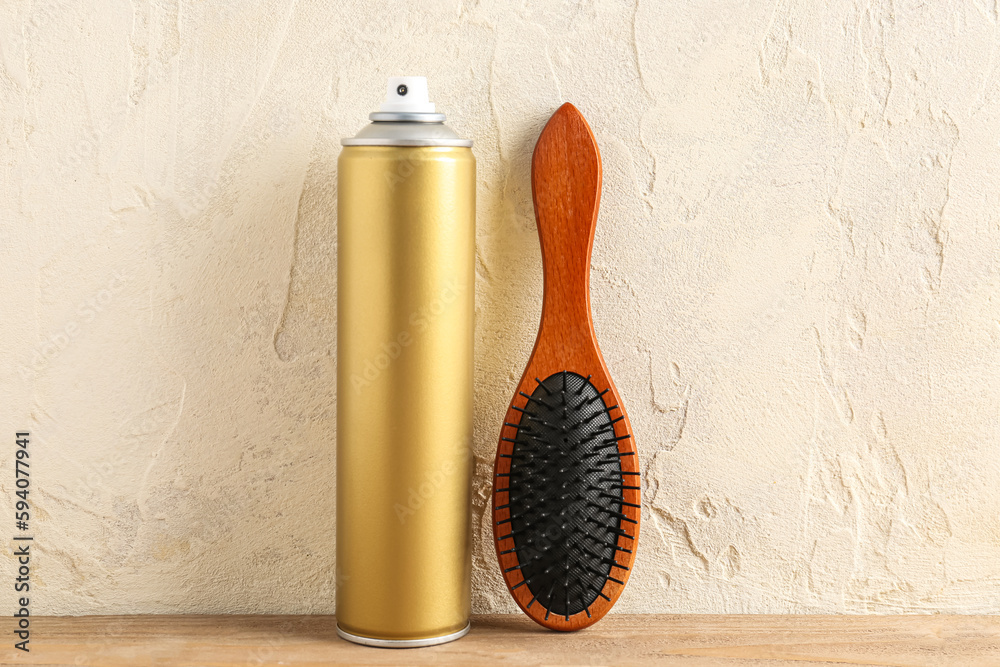 Bottle of hair spray and brush on table near light wall