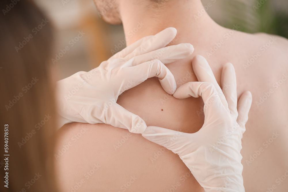 Dermatologist examining mole on young mans back in clinic, closeup