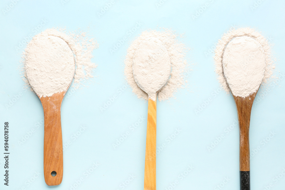 Different wooden spoons with wheat flour on blue background, closeup